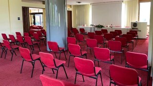A conference room with rows of red chairs, a white table with a podium, and a large pillar.