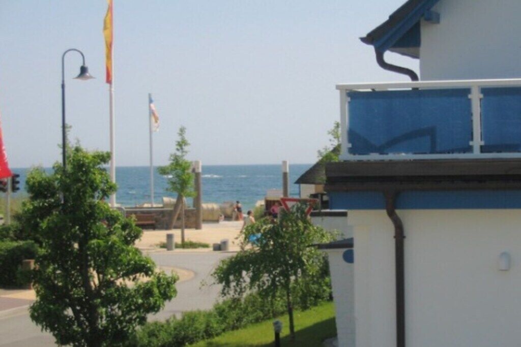 A coastal building with a balcony overlooking the sea, a flagpole, and a street with pedestrians.