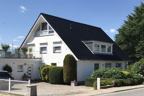 Ein zweistöckiges weißes Haus mit schwarzem Dach, einem sichtbaren Garage und einem weißen Zaun.