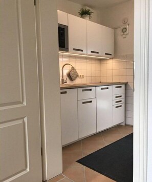 Eine Küche mit weißen Schränken, einer schwarzen Arbeitsplatte und einem schwarzen Teppich.