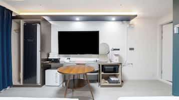 Habitación de hotel con televisión de pantalla plana, escritorio con computadora, cafetera y microondas.