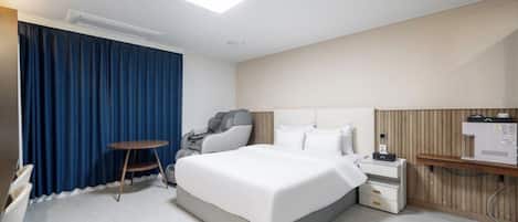 Habitación de hotel con cama, sillón de masaje, mesita, mesita de noche y calentador de pared.