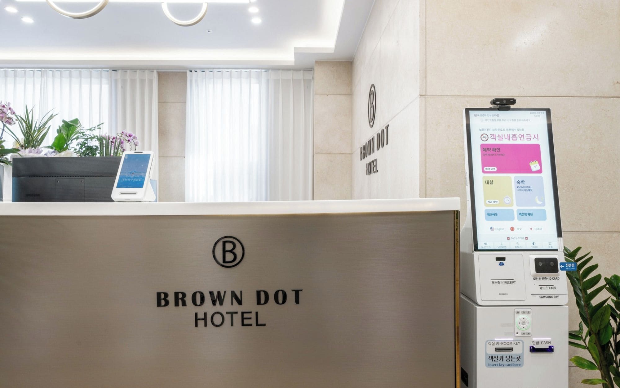 Un mostrador de recepción en Brown Dot Hotel con una pantalla digital y un lector de tarjetas Samsung Pay.