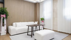 Un soggiorno moderno con un divano bianco, un tavolino e un poggiapiedi bianco. A sinistra, una pianta in vaso e, a destra, un oggetto decorativo.