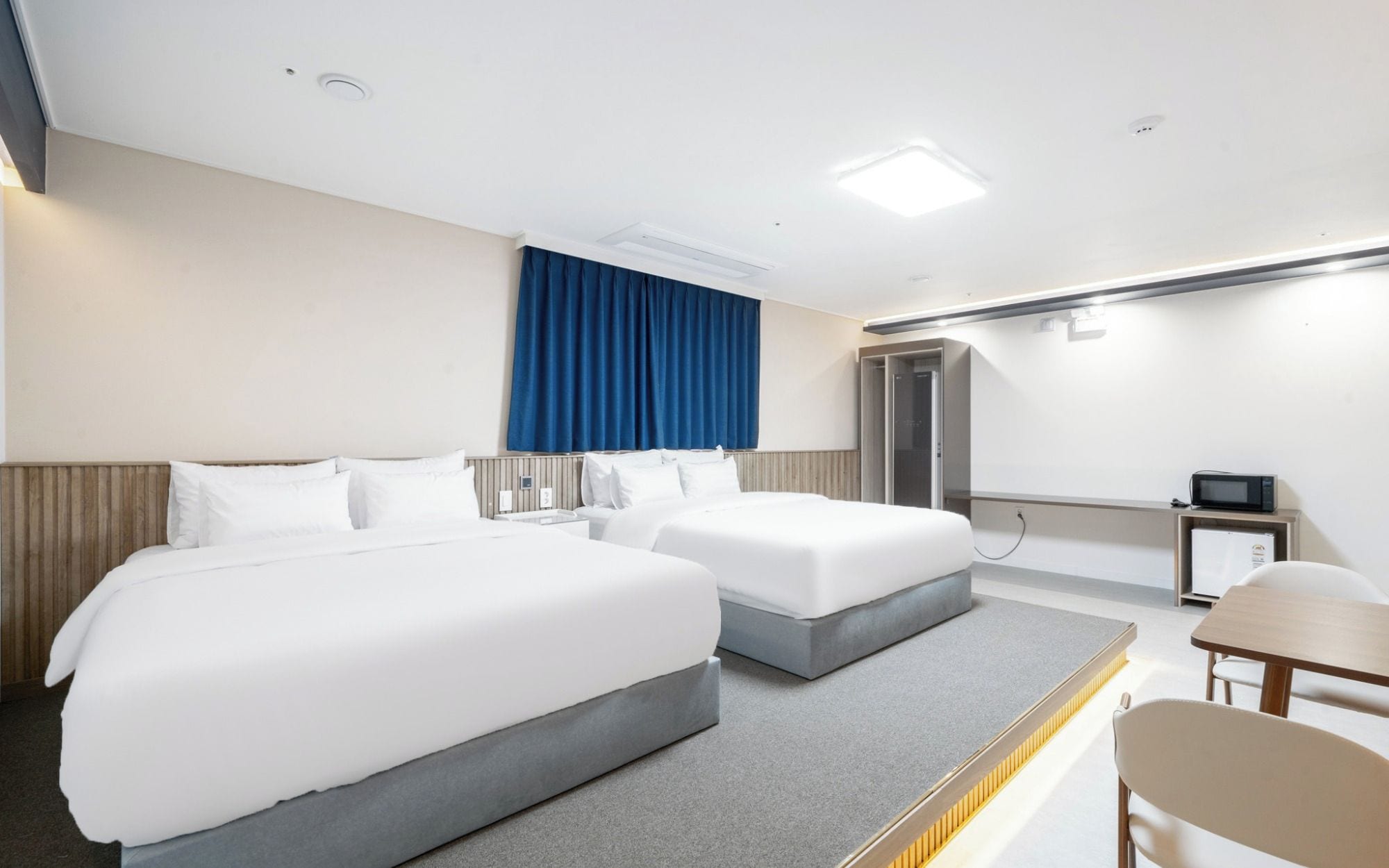 Una habitación de hotel con dos camas, un escritorio, una silla, un microondas y una puerta.