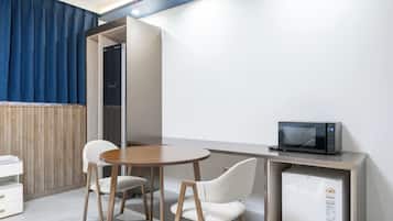 Una moderna camera d'albergo con un tavolino rotondo in legno, due sedie bianche, una televisione a schermo piatto e un mini-frigo integrato.