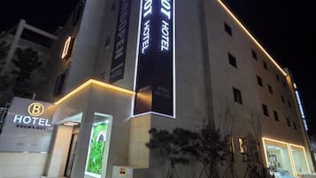 A hotel with a prominent sign, a vertical banner, and a well-lit entrance.
