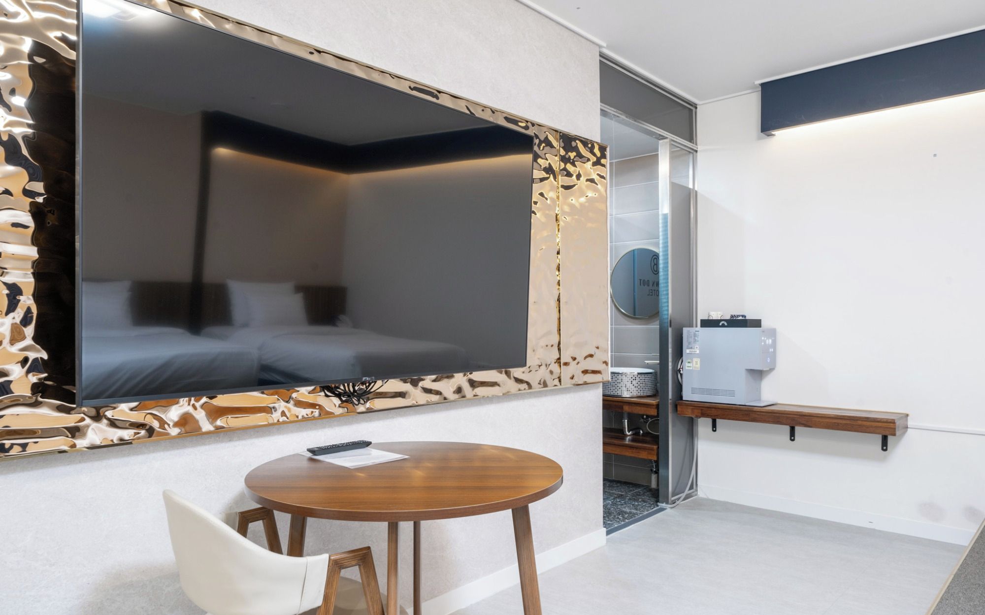 Una camera d'albergo con un letto grande, un tavolino piccolo e rotondo, una sedia, una scrivania con un computer e un grande specchio.