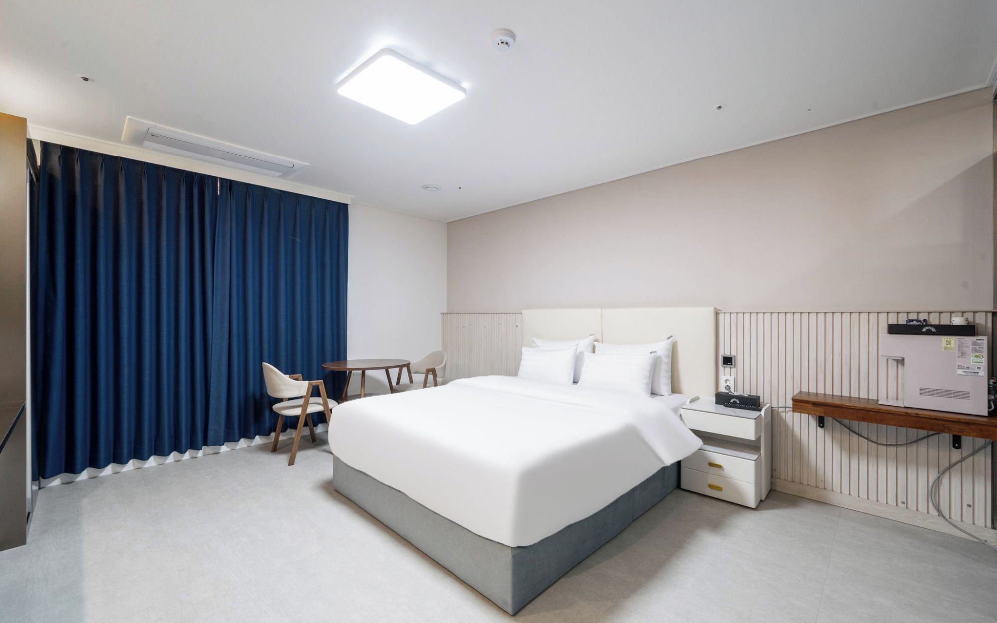 A hotel room with a bed, bedside table, chair, and a desk with a chair.