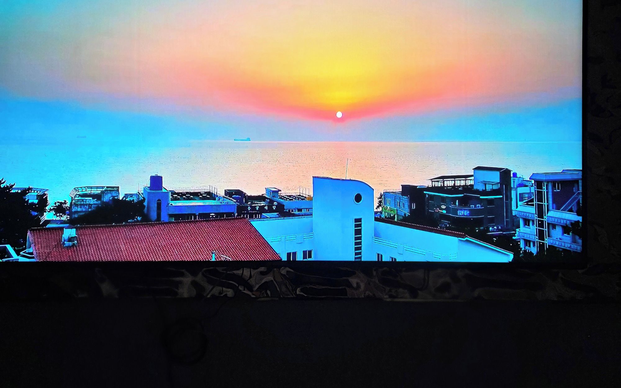 Un paisaje urbano costero con edificios y un atardecer sobre el mar.