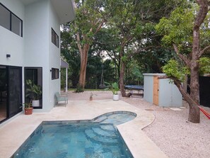 Una casa moderna con piscina, rodeada de árboles y un área de grava.