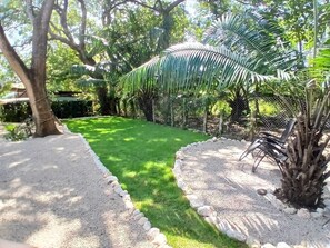 Ein gepflegter Garten mit Rasen, Kieswegen und verschiedenen Pflanzen, darunter eine Palme.