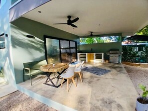 Eine Terrasse im Freien mit Esstisch, Stühlen, Deckenventilator und Grillbereich.