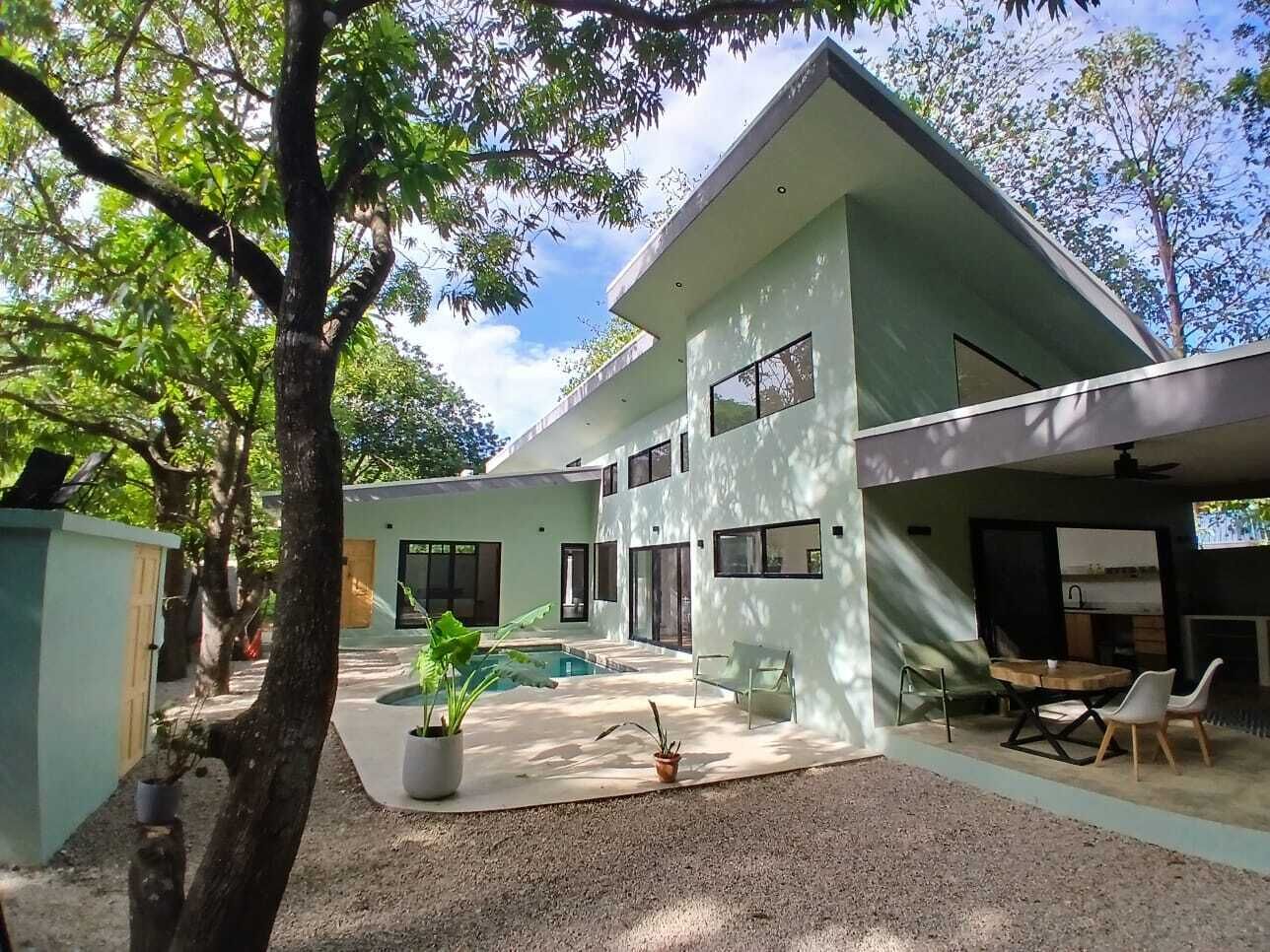 A modern two-story house with a swimming pool, outdoor seating, and a large tree.