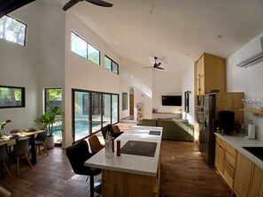 A modern kitchen with a dining area, large windows, and a ceiling fan. - Between Waves & Woods – Your Luxury Escape by the Ocean (Sámara)