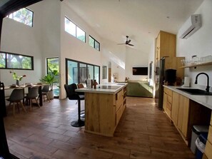 A spacious kitchen with wooden flooring, a central island, and a dining area with chairs and a table. - Between Waves & Woods – Your Luxury Escape by the Ocean (Sámara)