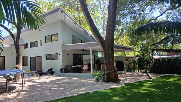 Ein modernes, zweistöckiges Haus mit einer überdachten Terrasse, Sitzgelegenheiten im Freien und einem gepflegten Rasen.