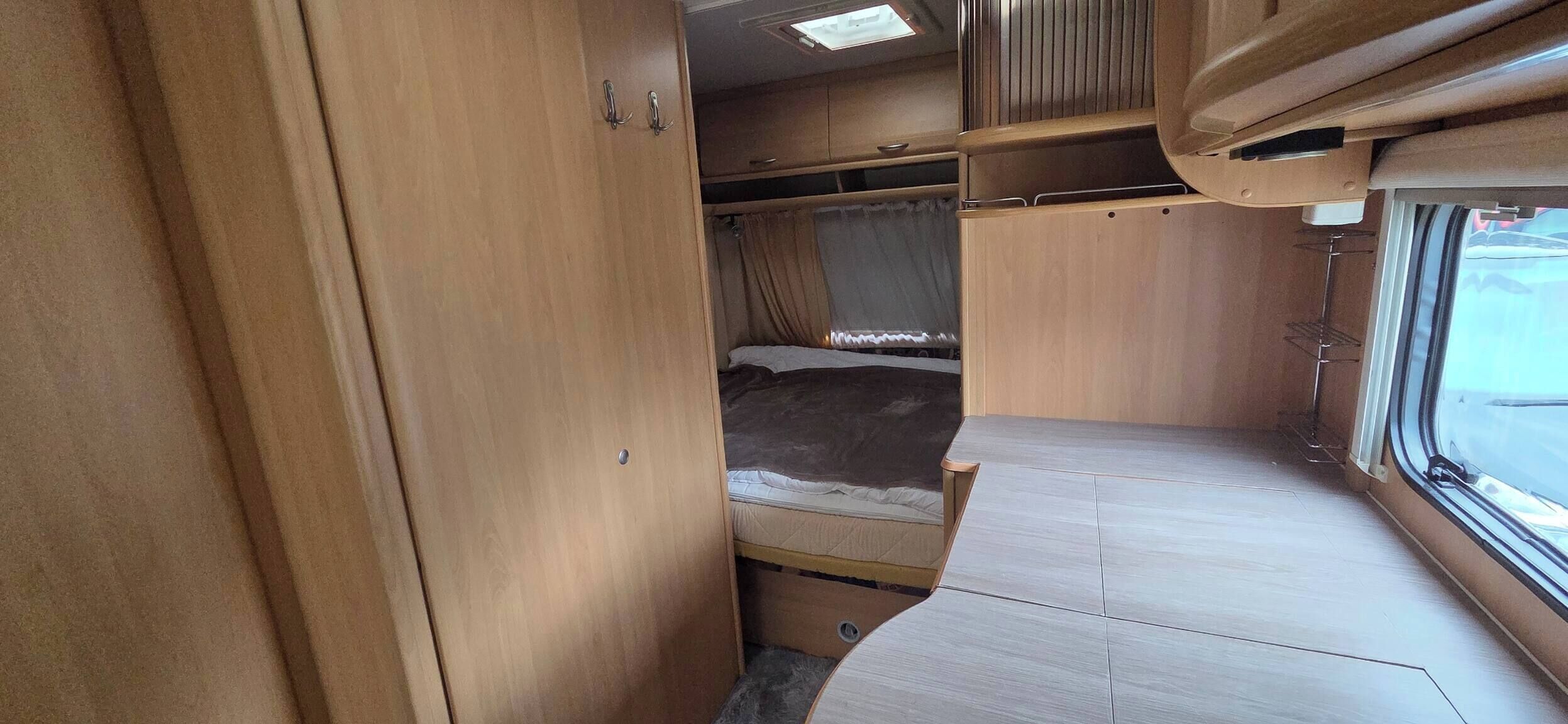 Un intérieur de camping-car compact comprenant un lit, des placards de rangement et une fenêtre.