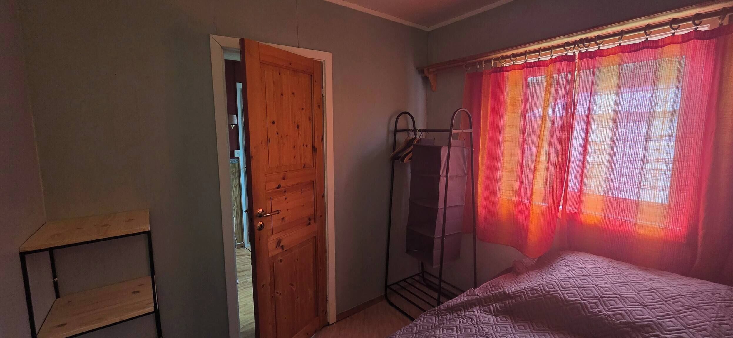 A bedroom with a wooden door, a metal drying rack, and a bed with a patterned bedspread.