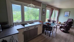 A kitchen with a large window, wooden cabinets, a dining table with chairs, and a fireplace.