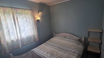 Ein Schlafzimmer mit einem Einzelbett, einem Nachttisch, einer Lampe und einem Fenster mit blumigen Vorhängen.