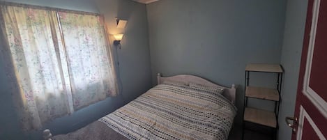 A bedroom with a single bed, a nightstand, a lamp, and a window with floral curtains.