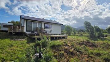 Ein eingeschossiges Haus mit einer Terrasse, einer überdachten Sitzgruppe und Blick auf die Berge.