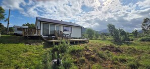 A single-story house with a deck, a covered outdoor seating area, and a mountain backdrop.