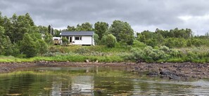 A house by a river with a rocky shoreline and dense greenery.