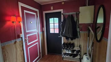 A hallway with a wooden floor, a black door, and a shoe rack with multiple pairs of shoes.