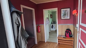 A hallway with a coat rack, a fire extinguisher, a desk with a backpack, and a framed picture on the wall.
