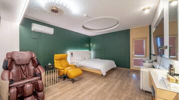 Habitación de hotel con cama, sillón de masajes, una mesita y un espejo.