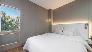 A modern hotel room with a large bed, a window with blinds, and a nightstand with a lamp.