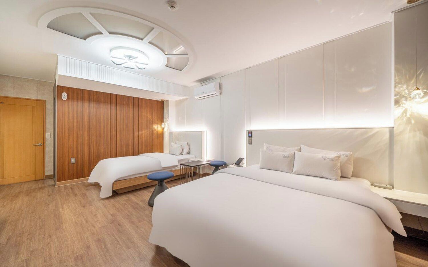 Habitación de hotel con una cama grande, una cama más pequeña, un escritorio y una lámpara en el techo.