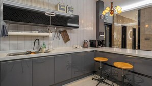 A modern kitchen with a built-in oven, a coffee machine, and a sink. There are two stools and a chandelier. - Andong Win Hotel (Andong)