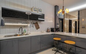 Una cocina moderna con horno empotrado, cafetera y lavaplatos. Hay dos taburetes y una araña.