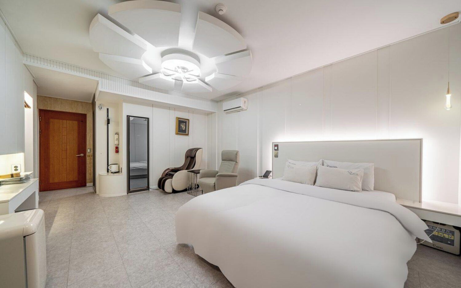 A modern hotel room with a large bed, a sitting area with chairs, a desk, and a door leading to a bathroom.