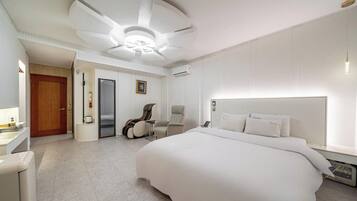 A modern hotel room with a large bed, a sitting area with chairs, a desk, and a door leading to a bathroom.