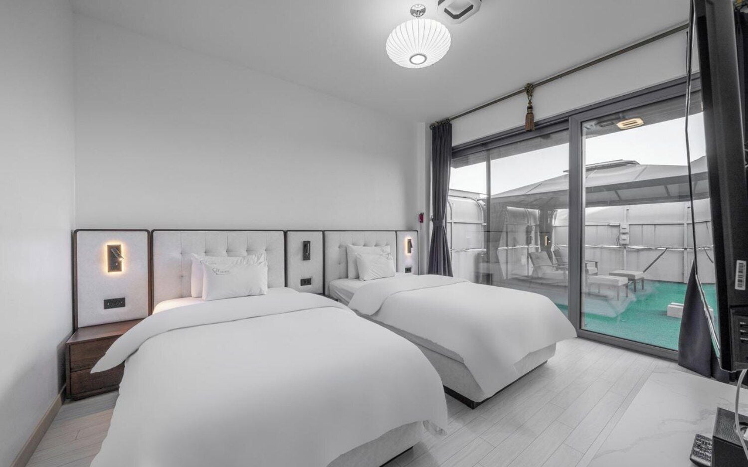Una habitación de hotel moderna con dos camas, un ventanal con vistas al exterior y una lámpara en el techo.