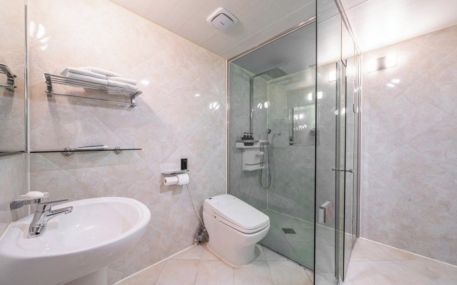 Un baño moderno con ducha envuelta en cristal, un lavamanos blanco y un inodoro.
