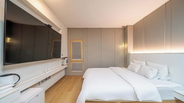 A modern bedroom with a large bed, a TV, a bedside table, and a wardrobe. - Andong Win Hotel (Andong)