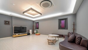 A modern living room with a flat-screen TV, a sofa, a small table, and a ceiling light fixture. - Andong Win Hotel (Andong)