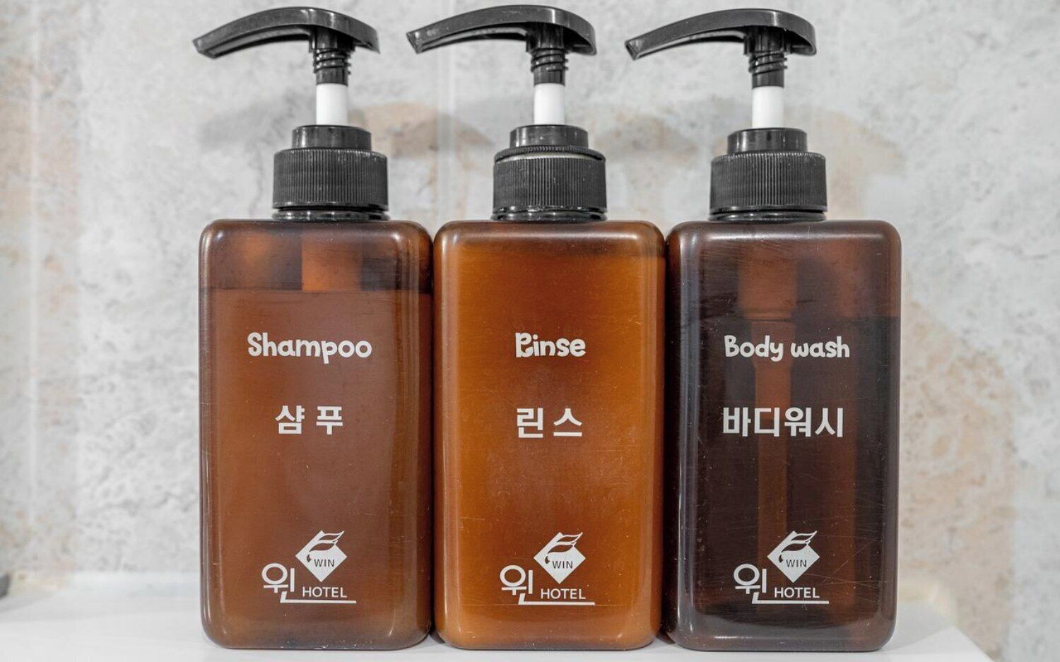 Three bottles of hotel toiletries: shampoo, body wash, and rinse.