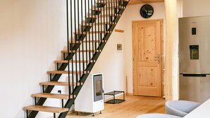 Una escalera con peldaños de madera y barandillas de metal negro, una puerta de madera, un refrigerador de acero inoxidable y un pequeño electrodoméstico blanco en el suelo.