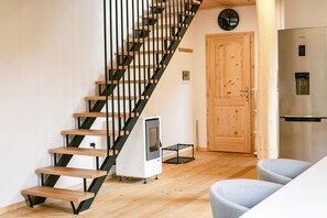 Eine Treppe mit Holzbeschlägen und schwarzen Metallgeländern, eine Holztür, ein Edelstahlkühlschrank und ein kleines weißes Gerät auf dem Boden.