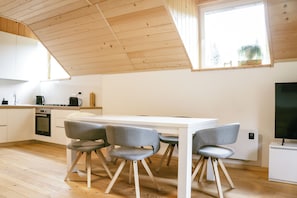 Eine moderne Küche mit weißer Arbeitsplatte, integriertem Backofen und einem Essbereich mit weißem Tisch und vier grauen Stühlen.