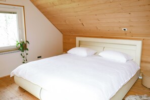Une chambre avec un plafond en bois, un grand lit avec une literie blanche, une fenêtre avec une plante et une petite table de chevet.