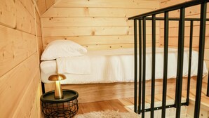 Un interior de madera con una cama, una mesita redonda con una lámpara y una alfombra blanca y mullida.