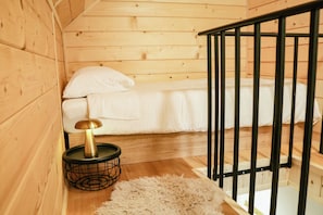 Ein Holzinterieur mit einem Bett, einem kleinen runden Tisch mit einer Lampe und einem weißen, flauschigen Teppich.