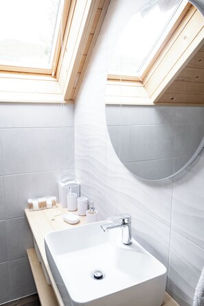 Un bagno moderno con un lucernario, un lavandino bianco e un mobile bagno in legno.